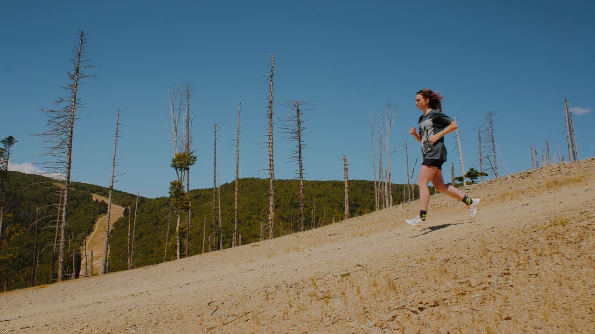 A lone woman enjoys a summer run on a scenic hillside path surrounded by nature and clear blue skies.